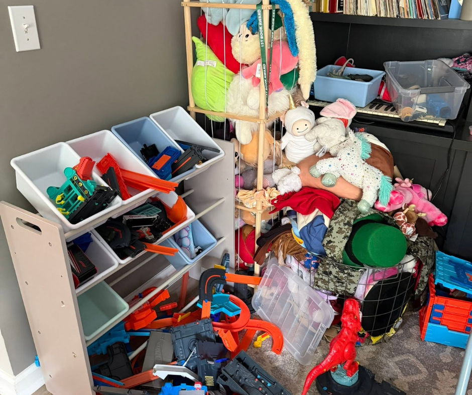 Cluttered playroom with tipped toy shelf, scattered toys, and a stuffed animal pile on the floor.