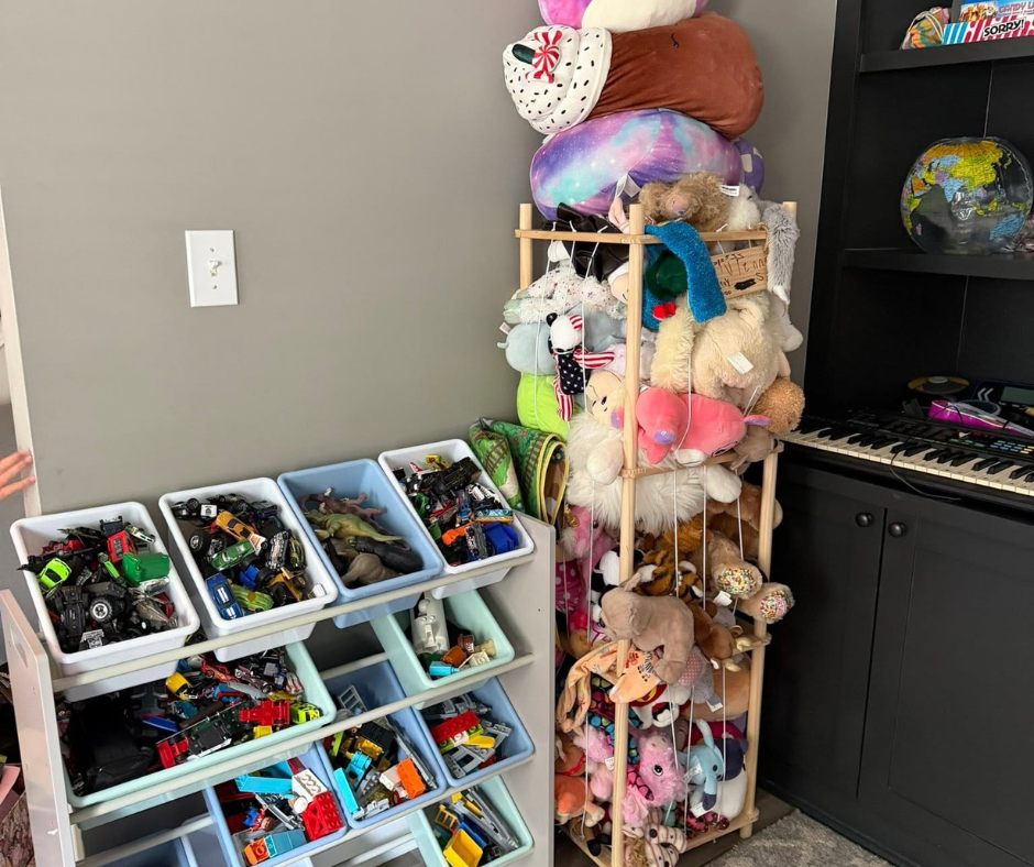 Children’s toy room with bins of toys, a stuffed-animal tower, and a black shelf against a gray wall