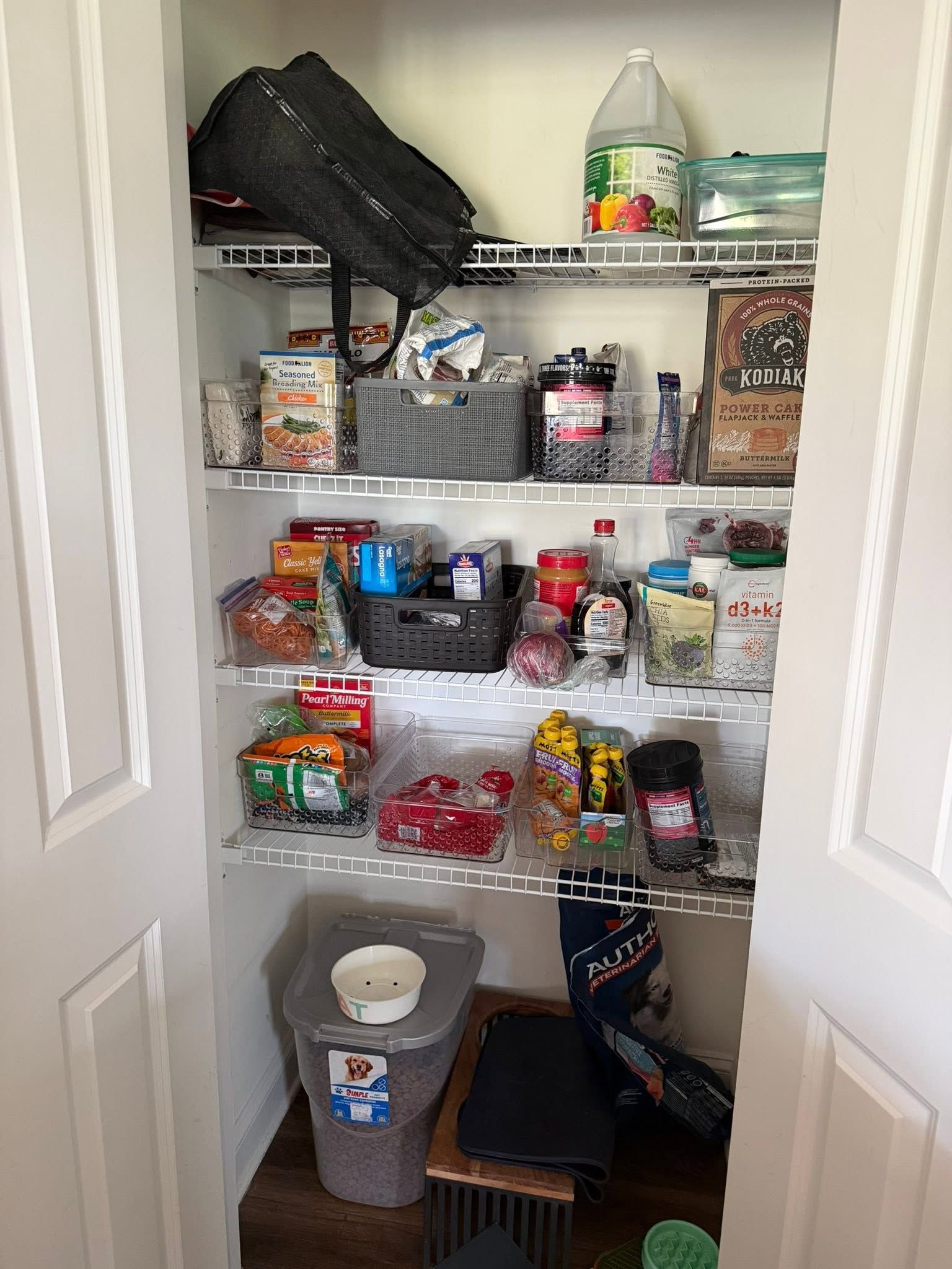 Open pantry closet with shelves of assorted snacks, jars, and containers, plus bins on the floor.