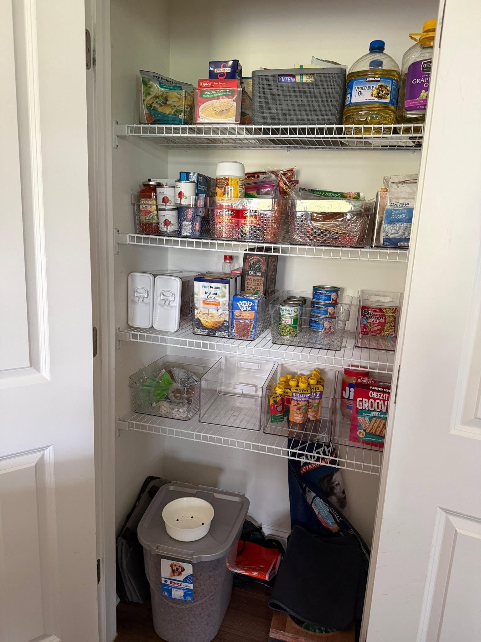 Pantry shelves stocked with canned goods, snacks, and bins, with a rice cooker on the floor below