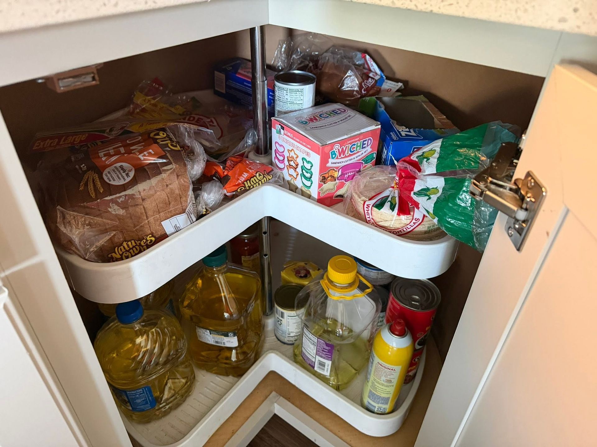 Open pantry shelf with bread, snacks, condiments, and bottled oil arranged on white lazy Susan shelves