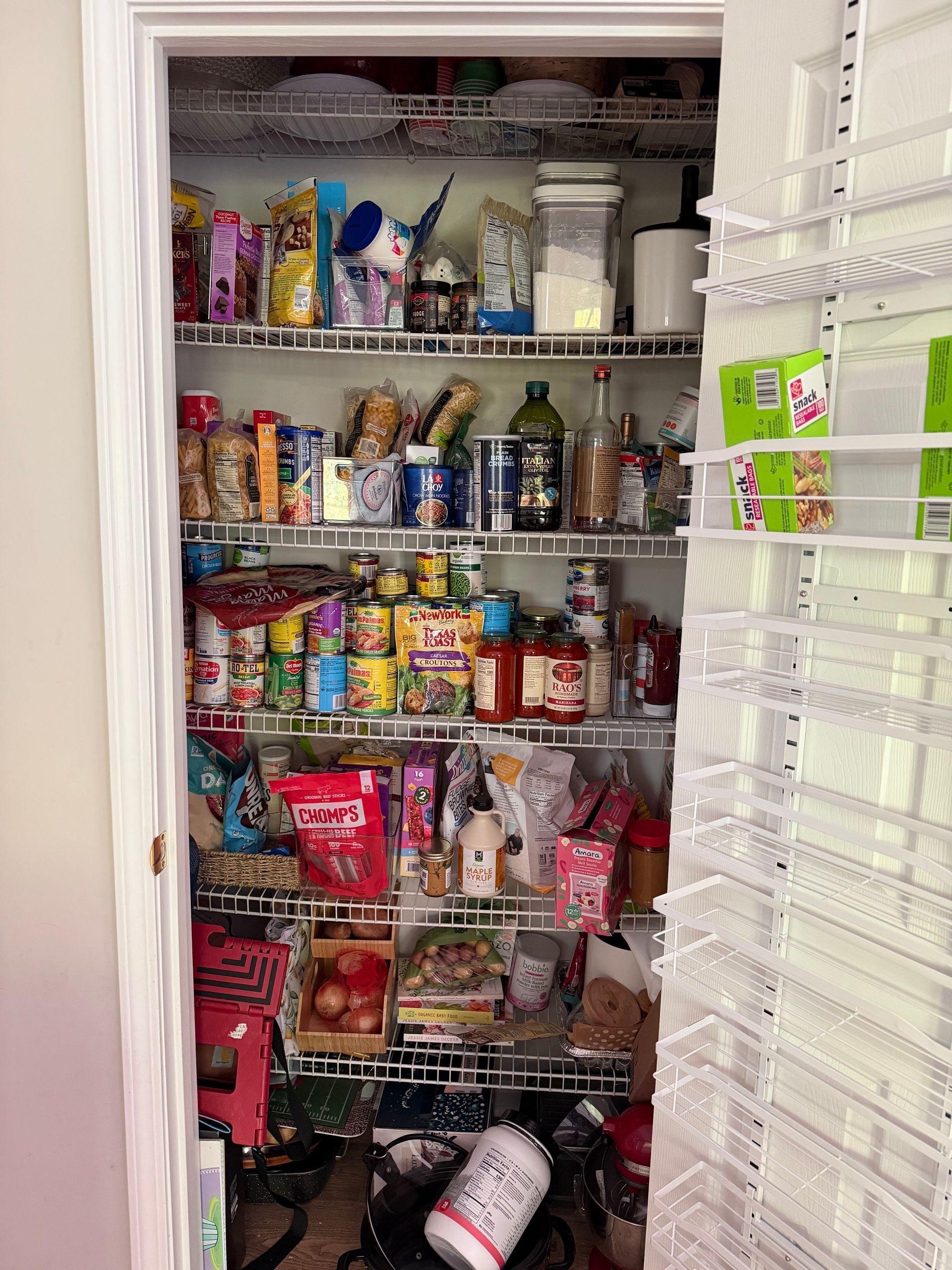 Packed pantry with shelves full of snacks, canned goods, jars, and bottles in a white closet-like storage space.