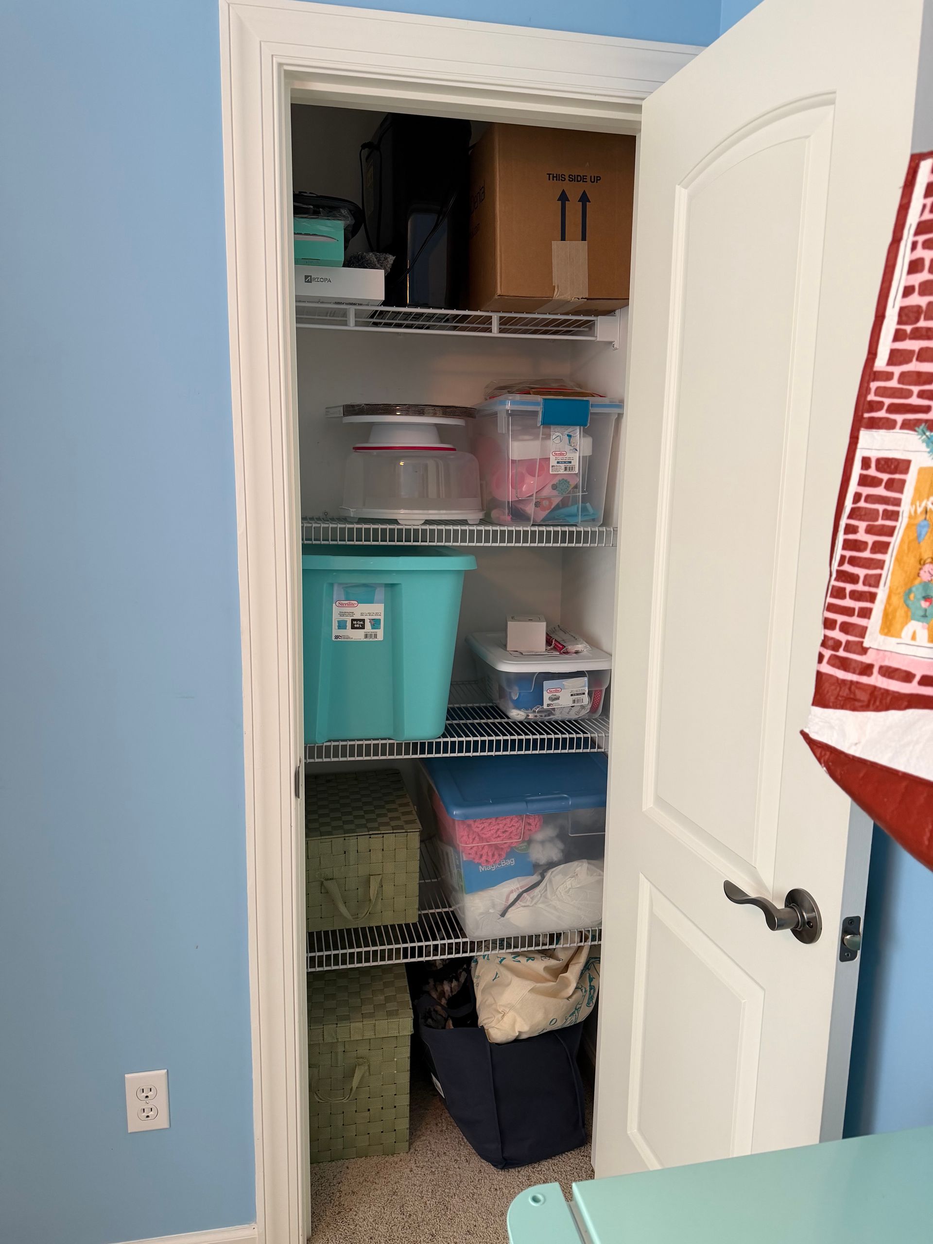 Open closet with white shelves and storage bins in a blue room, door partially open.