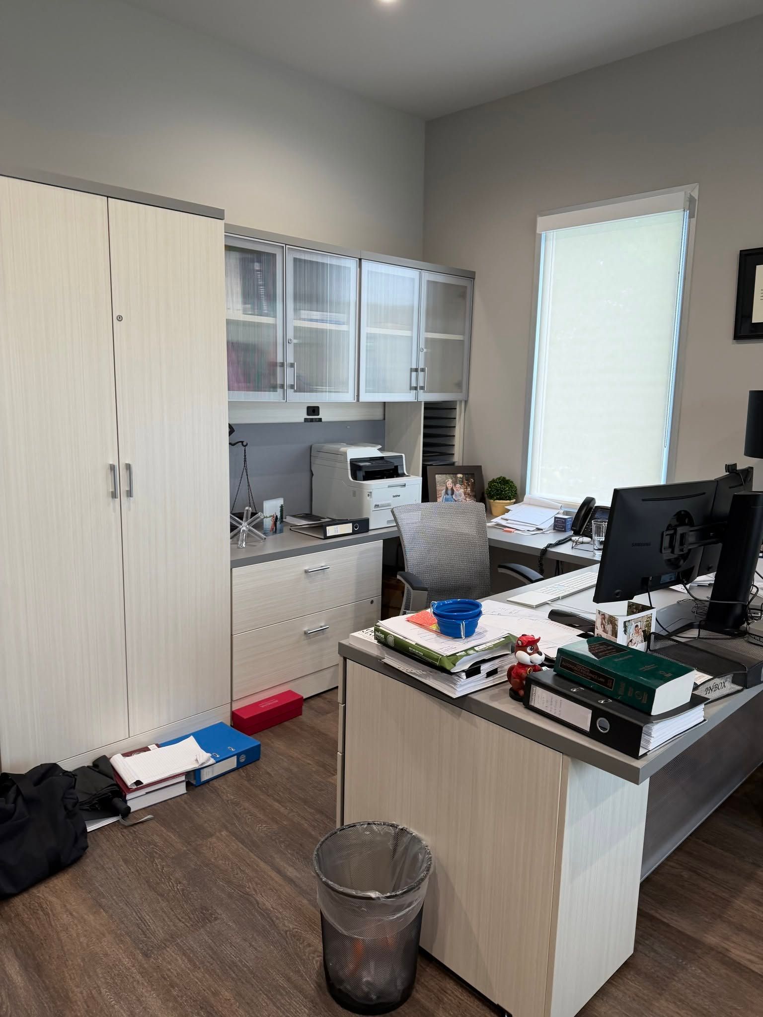 Office with desks, computer monitors, white cabinets, and a person seated at a cluttered workstation.