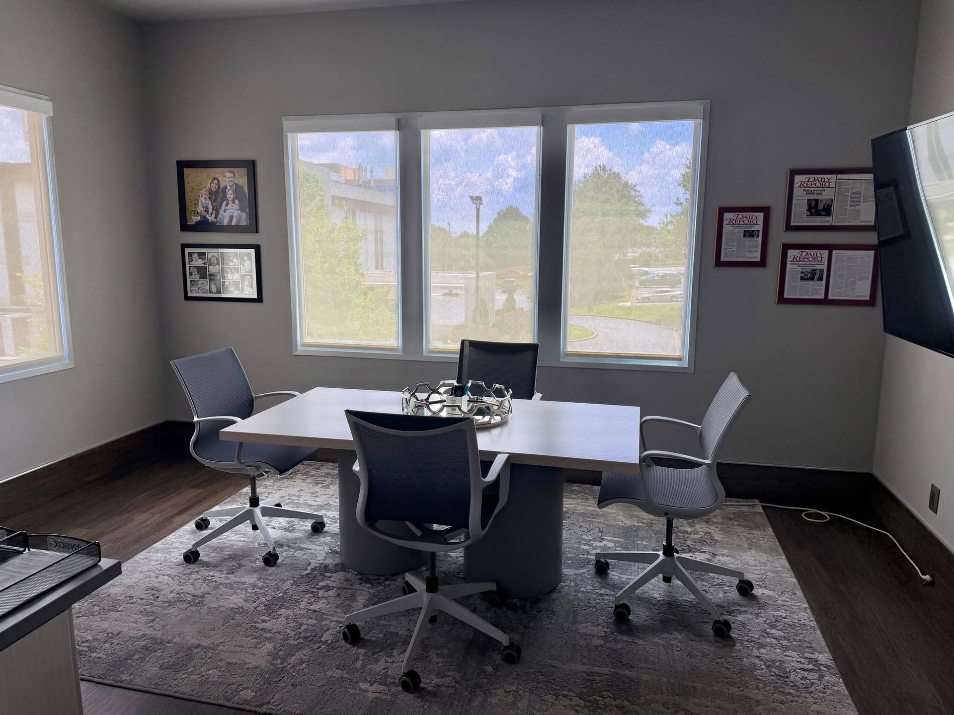 Bright office with table, four swivel chairs, gray rug, framed art, and three large windows.