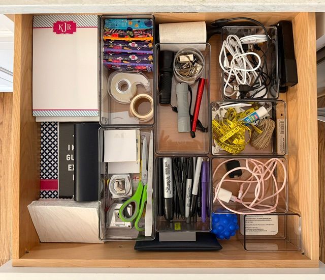 Wooden drawer organizer with assorted office supplies, cords, tape, scissors, and small tools arranged in compartments