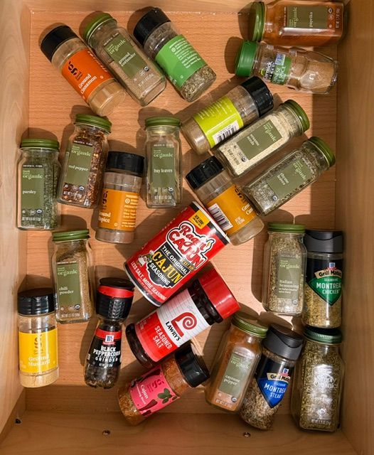 Scattered spice and seasoning jars in a wooden drawer, mostly green and black-labeled containers.