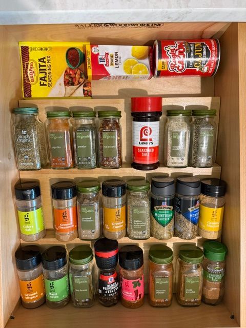 Spice rack cabinet filled with assorted jars and cans, neatly arranged on three shelves.