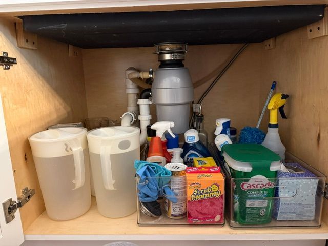Under-sink cabinet with cleaning supplies, paper towels, spray bottles, and a garbage disposal unit