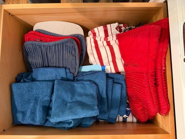 Folded blue, red, and striped towels stacked in a wooden drawer.