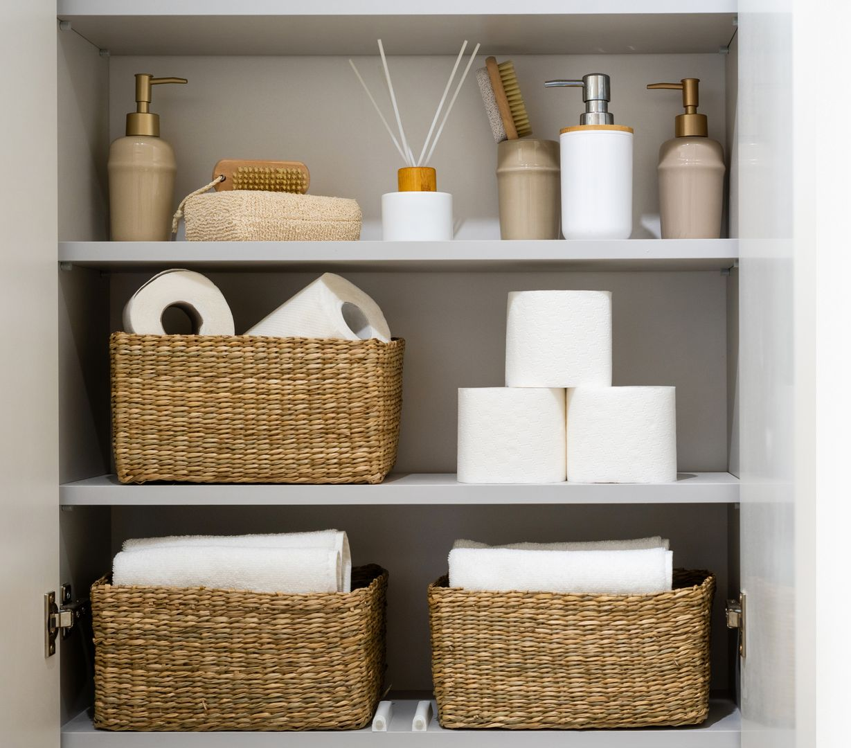 Neatly organized bathroom shelf with woven baskets, rolled towels, tissue rolls, and soap dispensers.