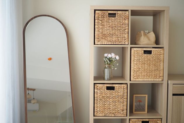 Tall arched mirror beside a wooden cubby shelf with woven baskets and decor in a bright room