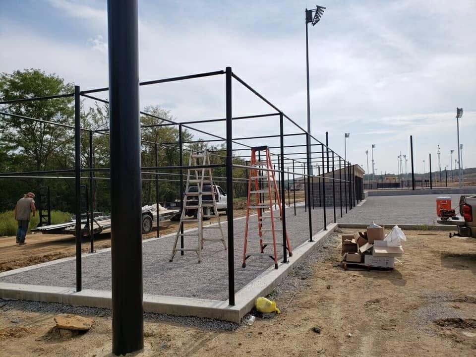 Construction site with black metal fence, ladders, and concrete slabs on a gravel lot