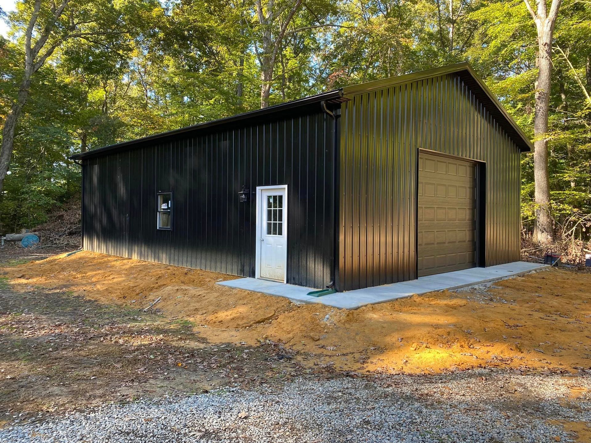 A black metal building with a garage door is sitting in the middle of a dirt field.