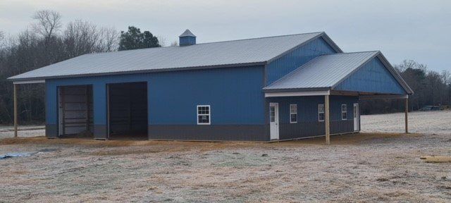 A blue barn with a white roof is in the middle of a field.