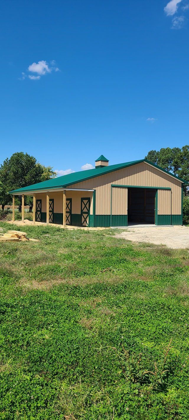 A large barn with a green roof is sitting in the middle of a grassy field.