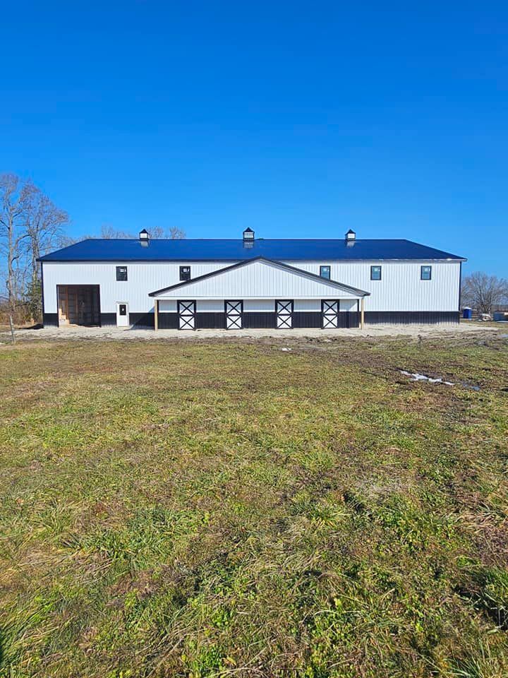 A large white barn is sitting in the middle of a grassy field.