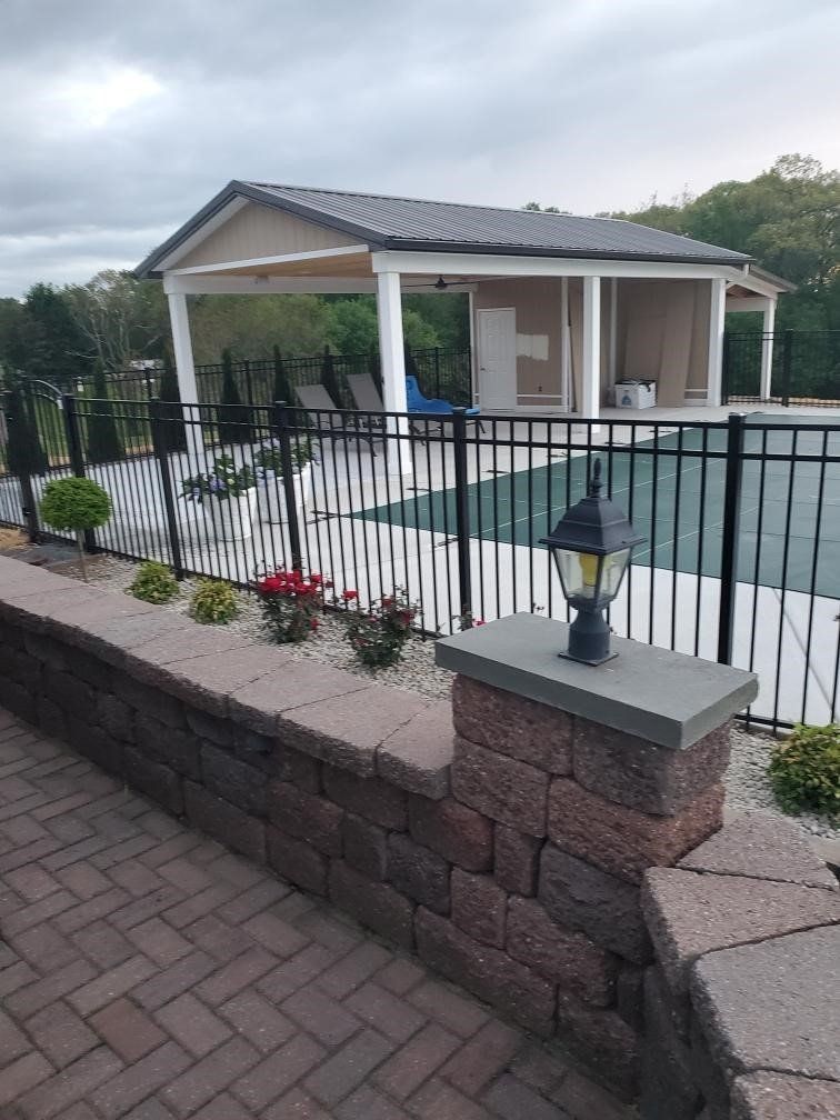 A fence surrounds a swimming pool with a pavilion in the background.