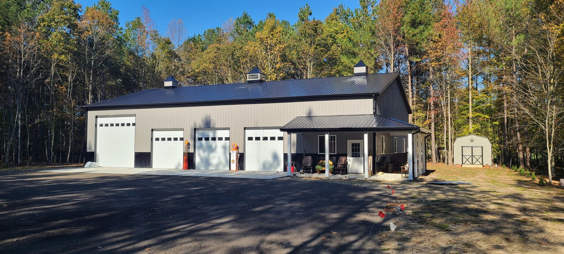 A large garage with a porch in the middle of a forest.