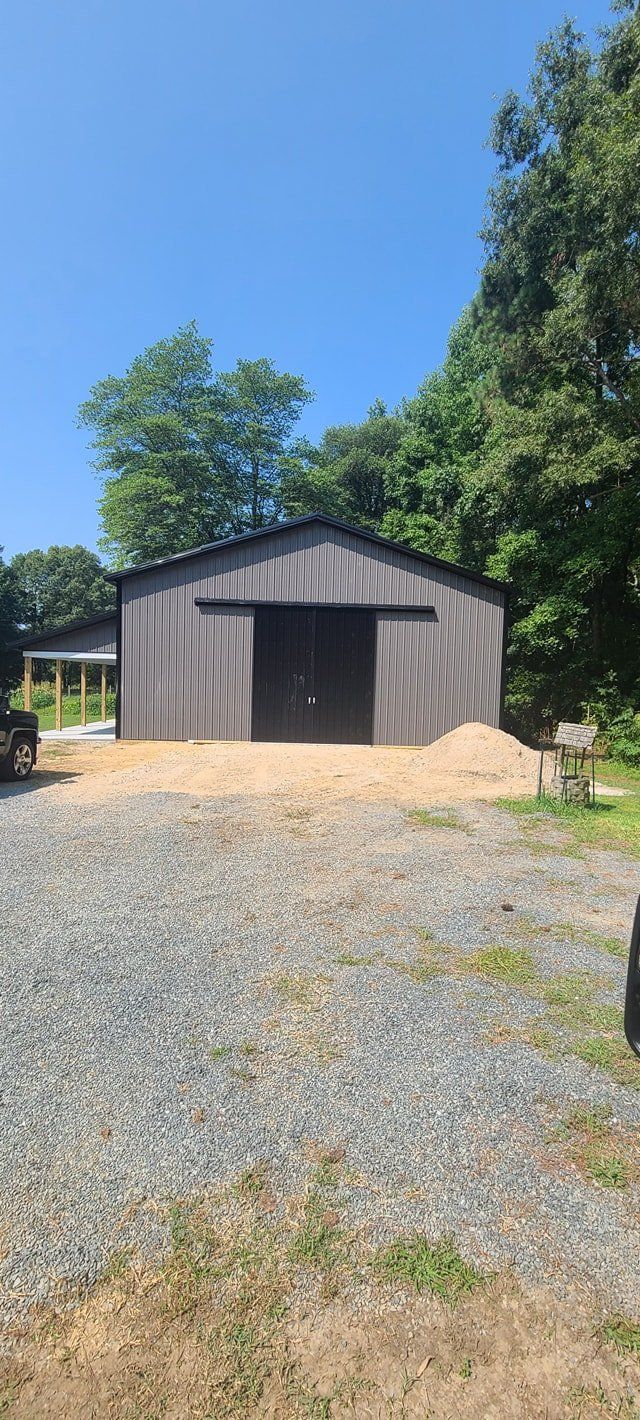 A large barn is sitting in the middle of a gravel lot.