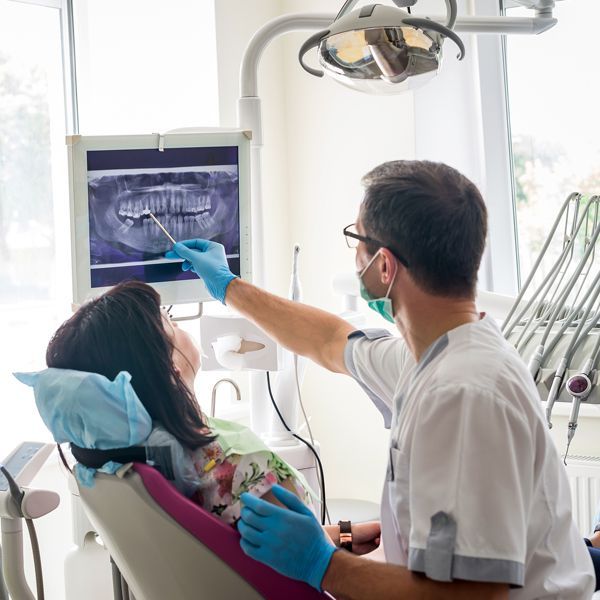 Dentist pointing at an X-ray while treating a patient in a bright dental clinic Dentist pointing at an X-ray while treating a patient in a bright dental clinic