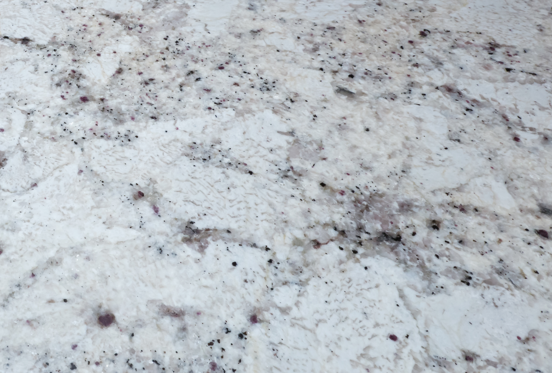 A close up of a white granite counter top with black spots.