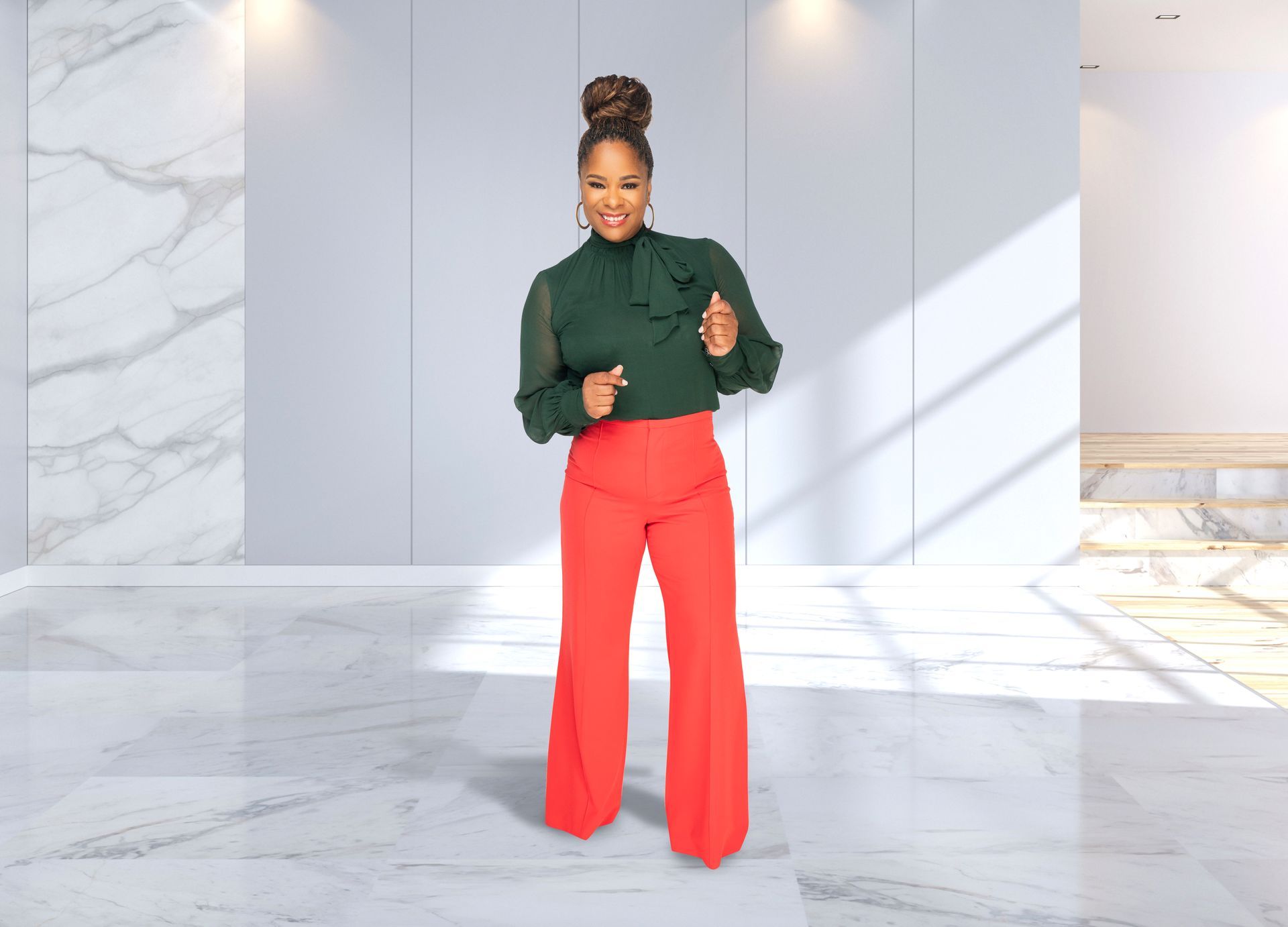 Coach Shermaine in a green top and red pants is standing in a room.
