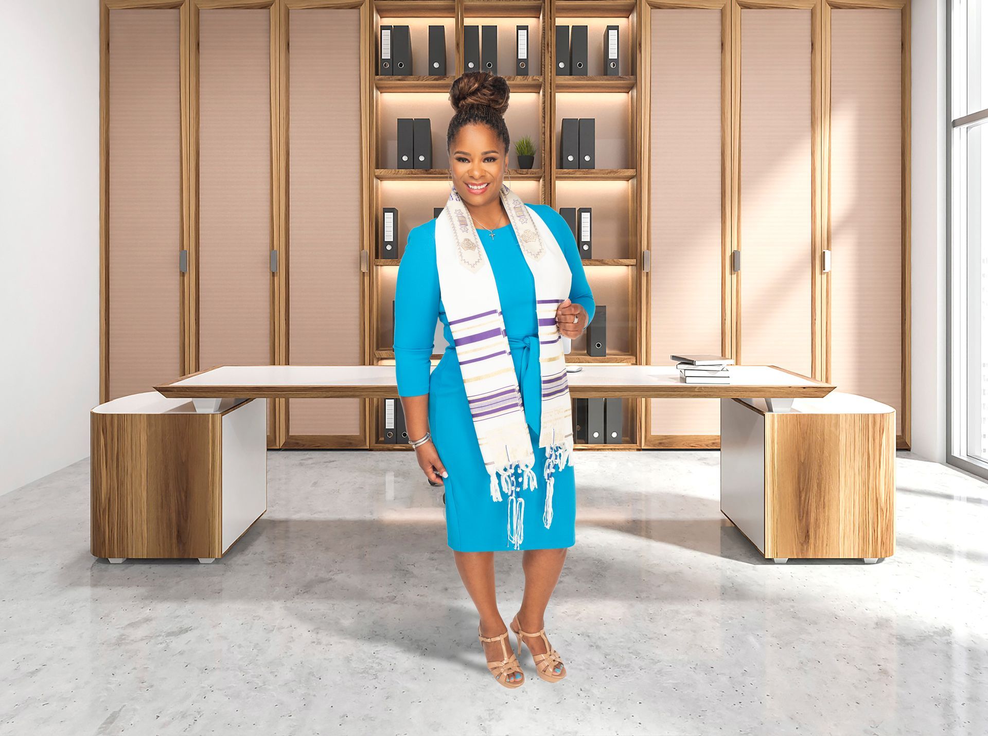 Coach Shermaine in a blue dress is standing in front of a desk.