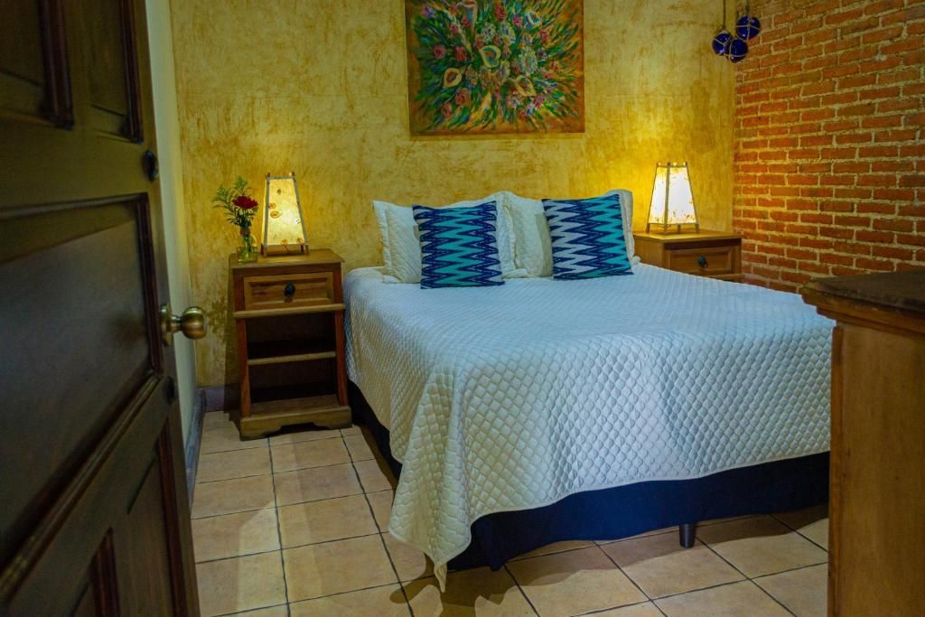 Habitación pequeña y acogedora con cama blanca, lámparas de noche, pared de ladrillo visto y suelo de baldosas.