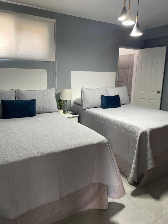 Dos camas individuales bien hechas en una habitación gris con lámparas y almohadas azules.
