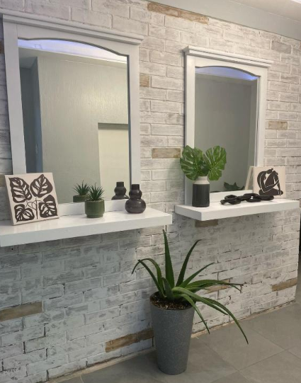 Pared de ladrillo blanco con espejos, estantes decorativos y plantas en macetas.