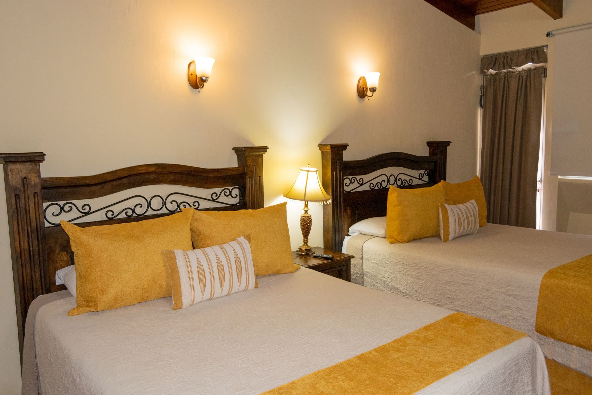 Dos camas impecablemente hechas en una habitación de hotel con iluminación cálida, detalles en amarillo y lámparas de pared.