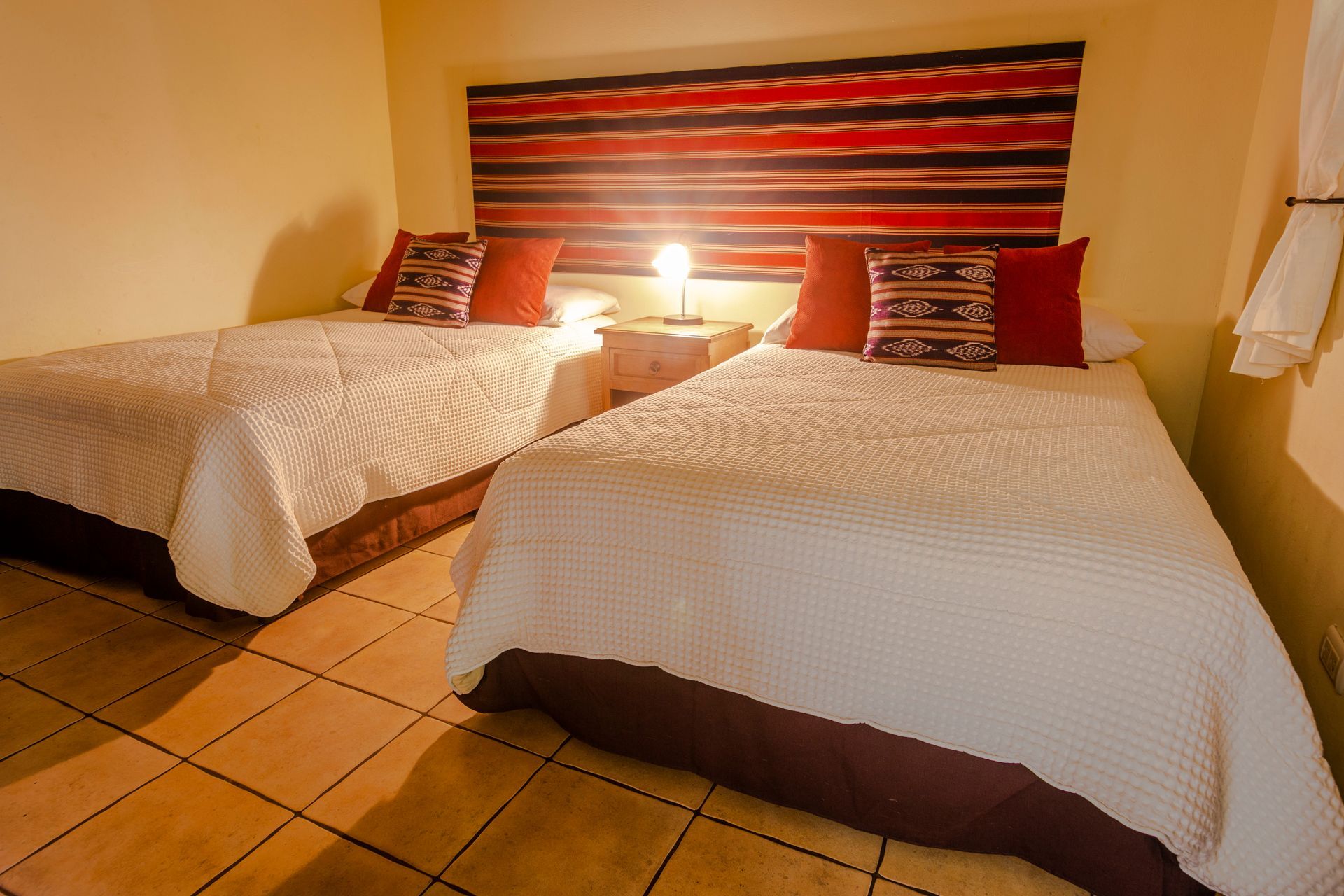 Dos camas individuales en una habitación de hotel con iluminación cálida, cabecero a rayas y suelo de baldosas.