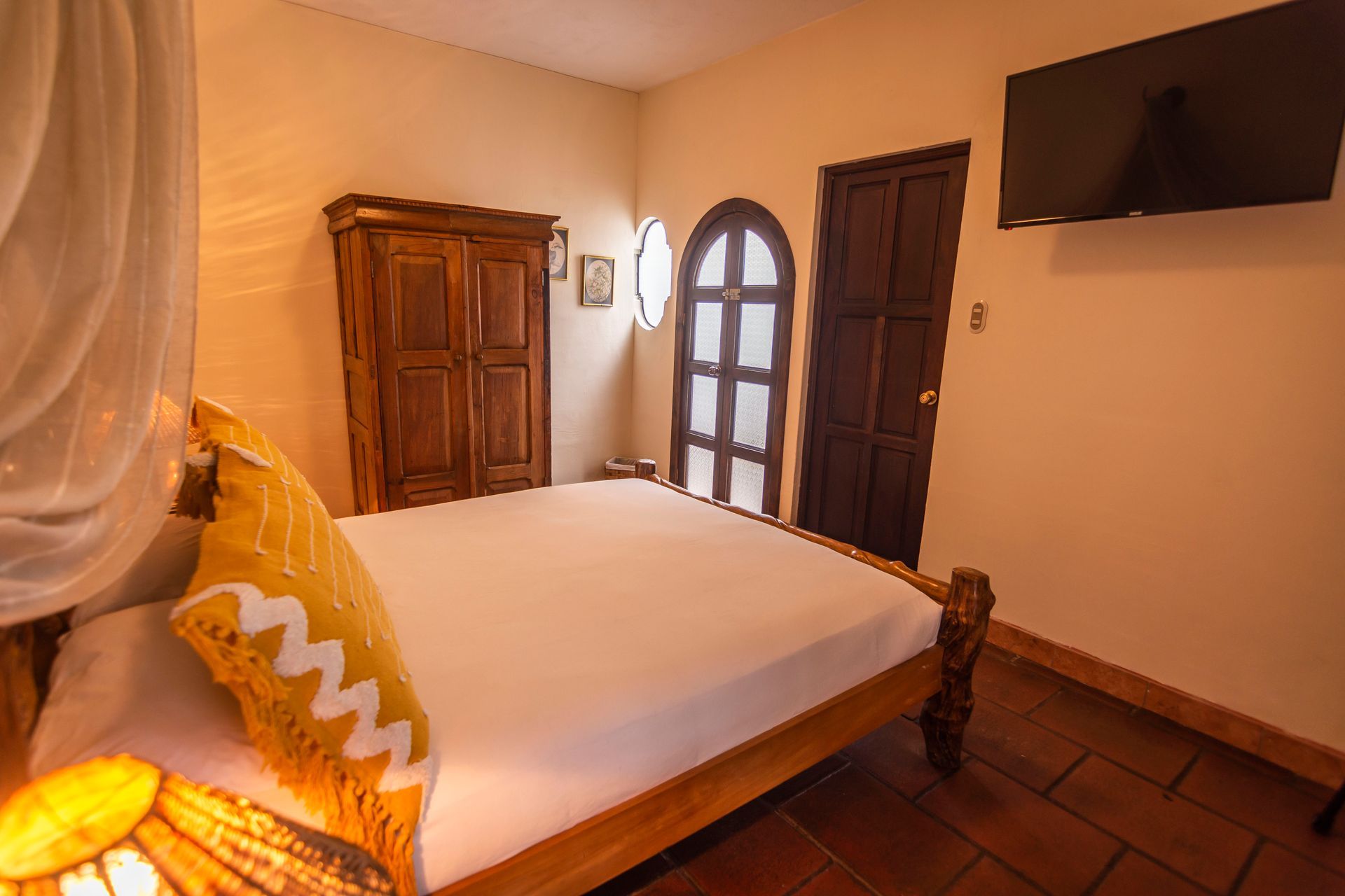 Habitación acogedora con cama de madera, armario, puerta arqueada y televisor montado en la pared con iluminación cálida.
