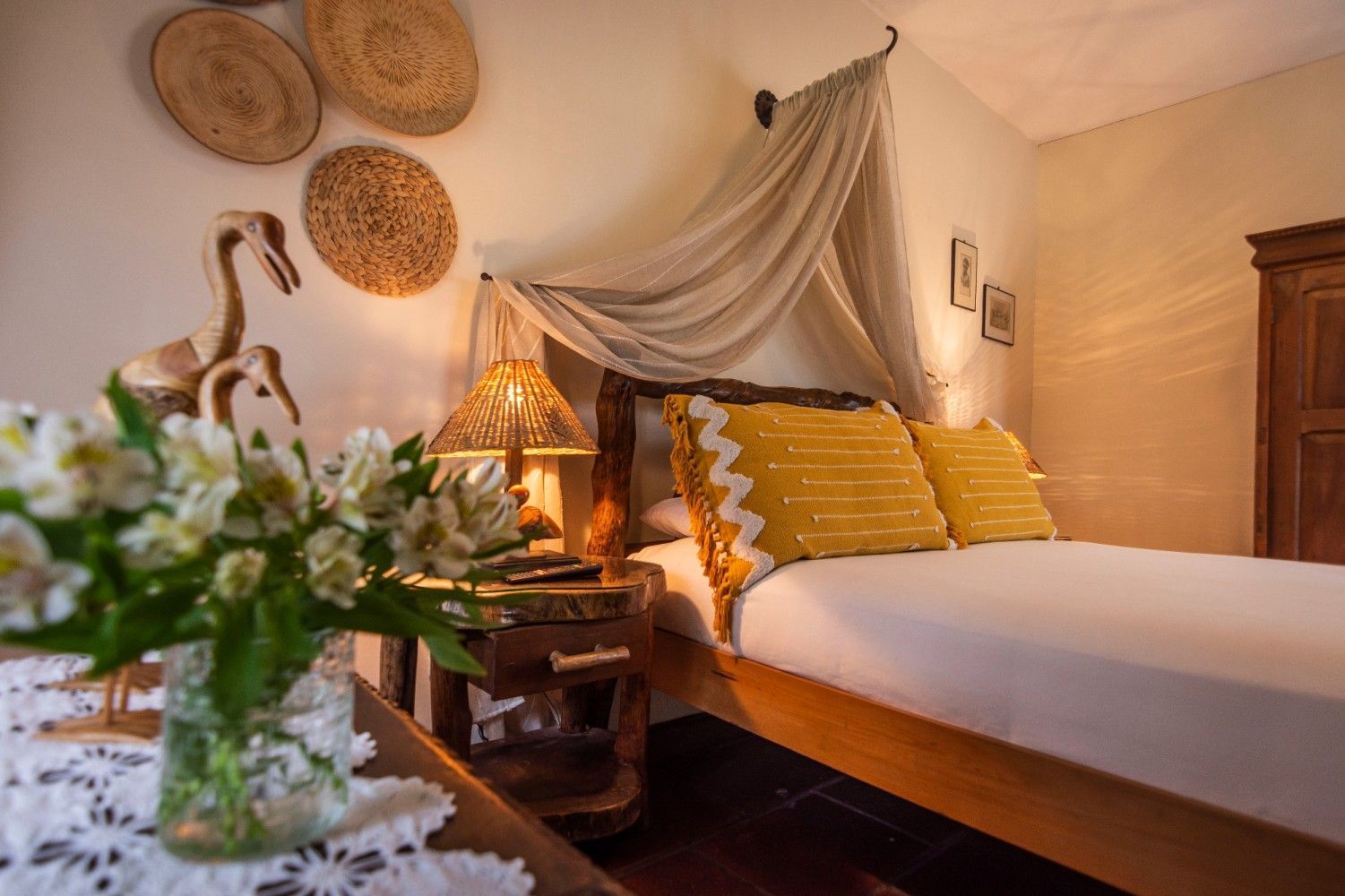Acogedora habitación con cama con dosel, almohadas amarillas, luz cálida y decoración tejida.