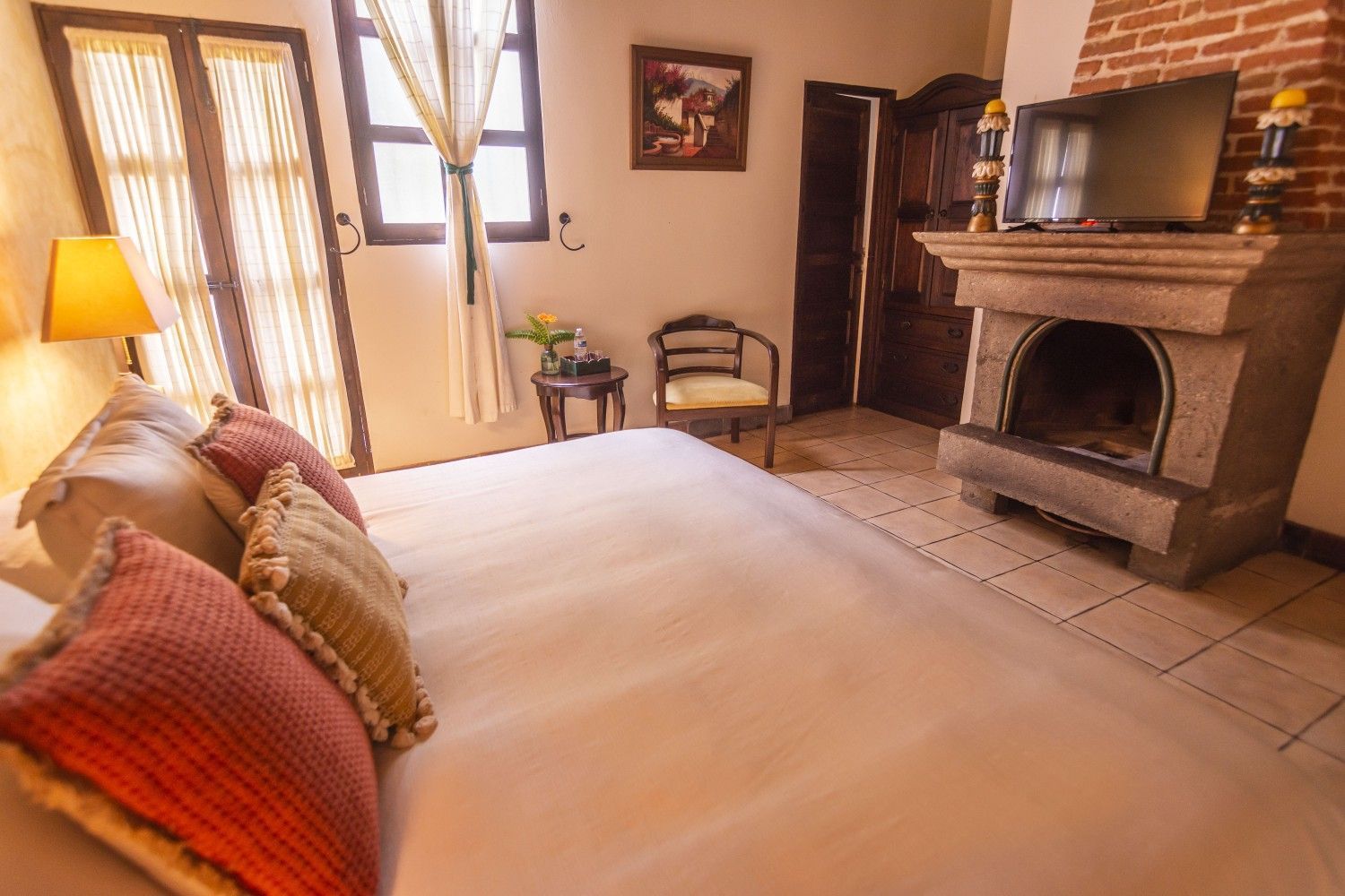 Habitación acogedora con una cama grande, chimenea de ladrillo, suelo de baldosas y lámparas cálidas junto a la ventana.
