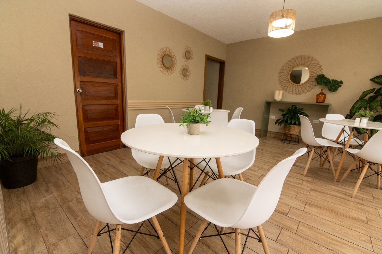 Comedor luminoso con sillas blancas, mesa redonda, suelo de madera y decoración de pared.