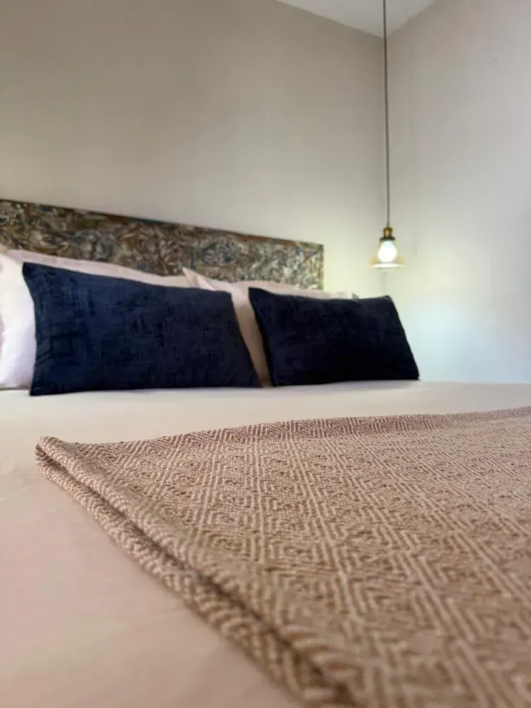 Cama impecable con almohadas azul marino y manta texturizada en un dormitorio luminoso y minimalista.