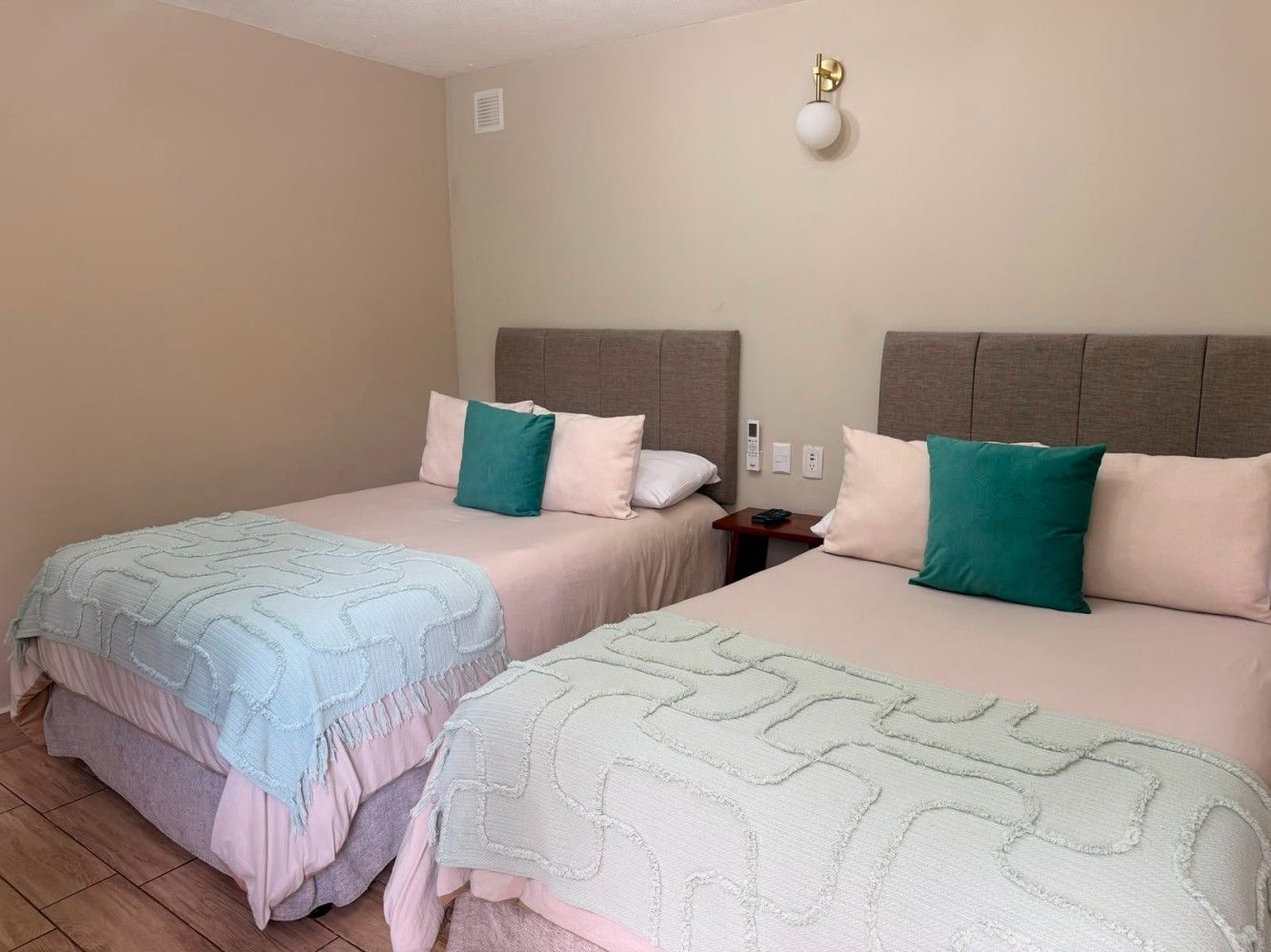Dos camas individuales en una habitación beige con ropa de cama turquesa y rosa y cabeceros grises.