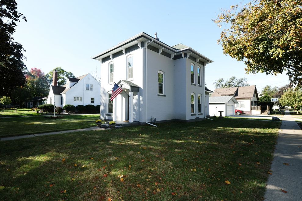 Gray two-story house with white trim on a grassy lawn in a quiet neighborhood, with trees and a driveway nearby
