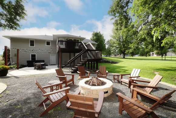 Backyard patio with fire pit, wooden chairs, and a deck beside a house
