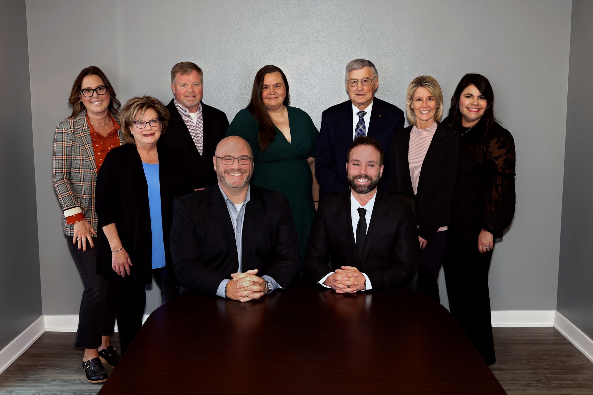 Group of eight people posing in business attire around a conference table in an office setting