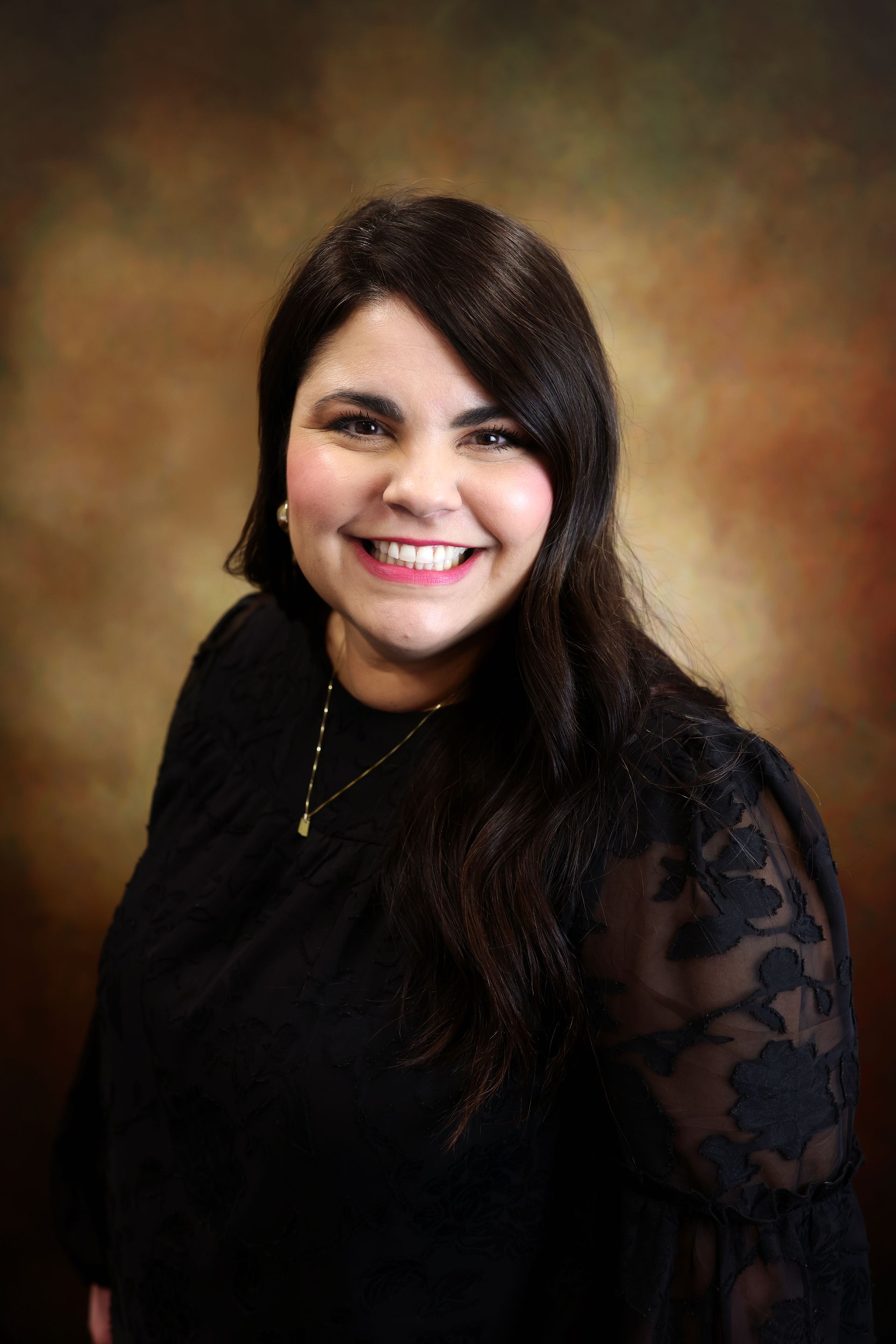 Smiling woman in a black top with lace sleeves against a warm brown studio backdrop