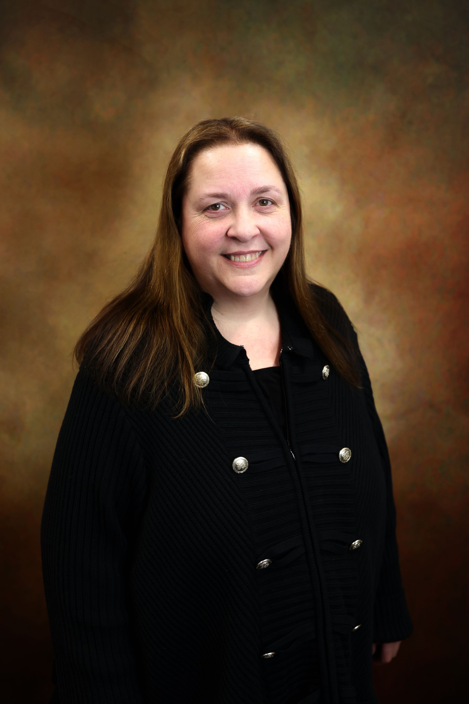 Smiling woman in a black coat posing against a brown studio backdrop