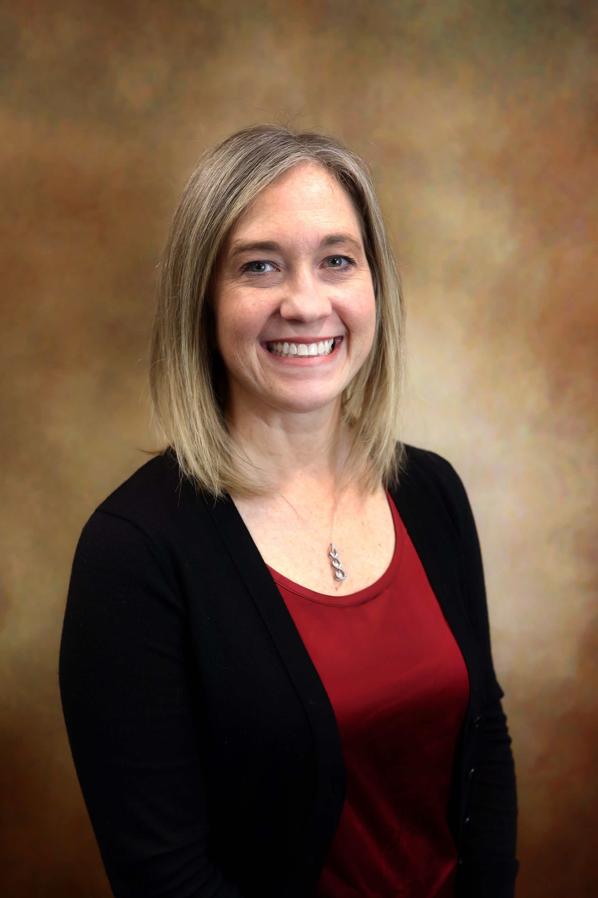 Smiling woman in a black cardigan and red top against a brown studio backdrop