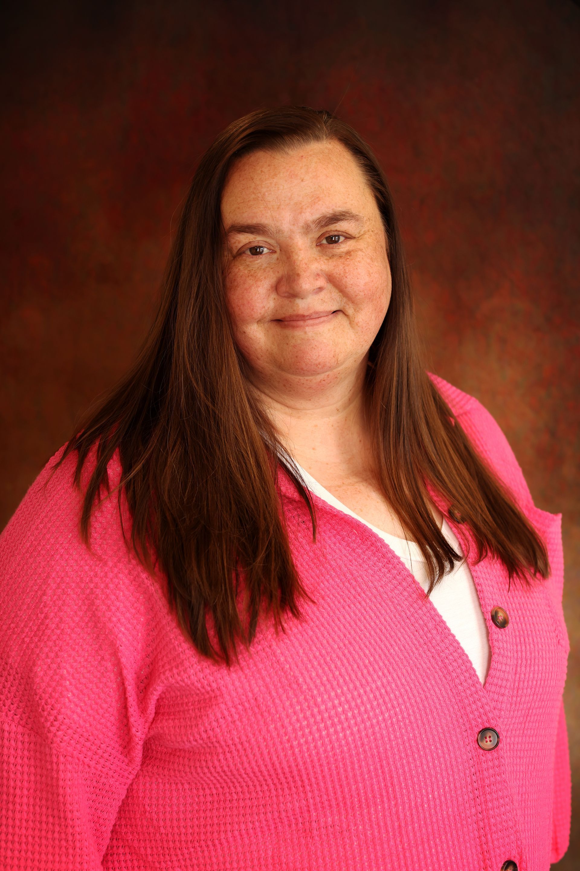 Woman in a bright pink sweater smiles against a dark studio backdrop.