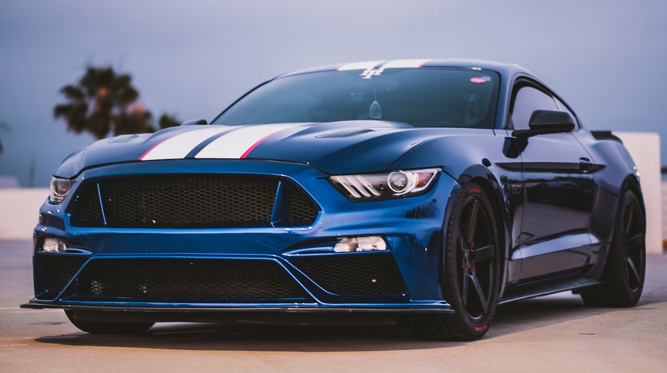 Blue sports coupe parked outdoors at dusk, low front-angle view with blurred palm trees in the background
