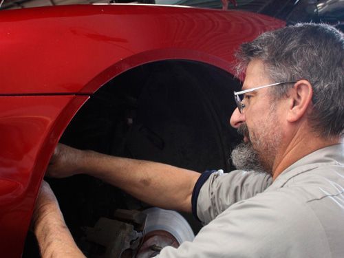A man is working on the fender of a red car.