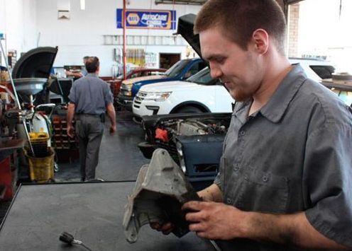 A man in a gray shirt is working on a car in a garage