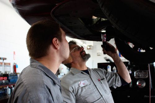 Two men are working on a car in a garage.